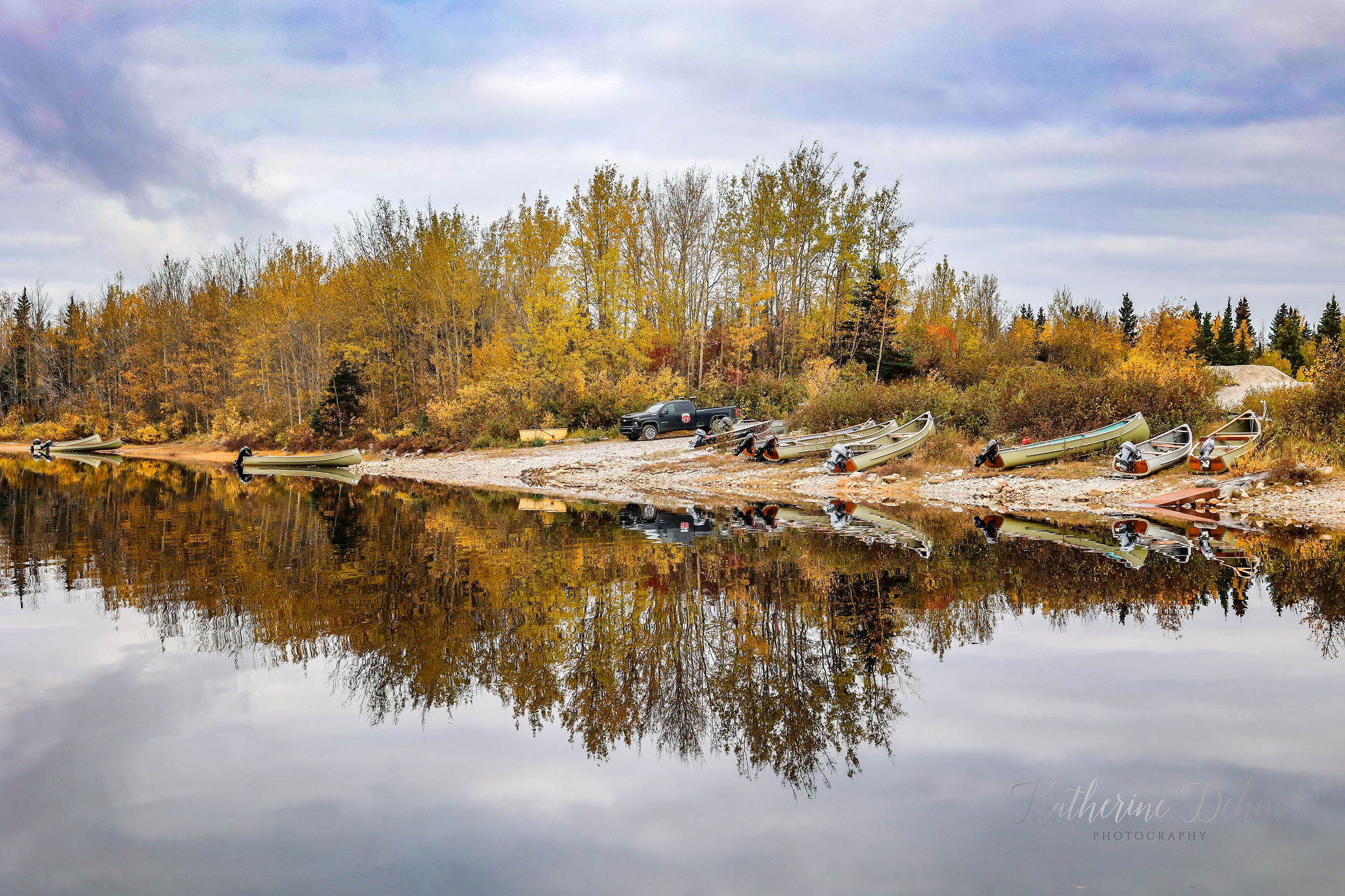 Freighter canoes drawn up on the shore, autumn trees reflected in still water