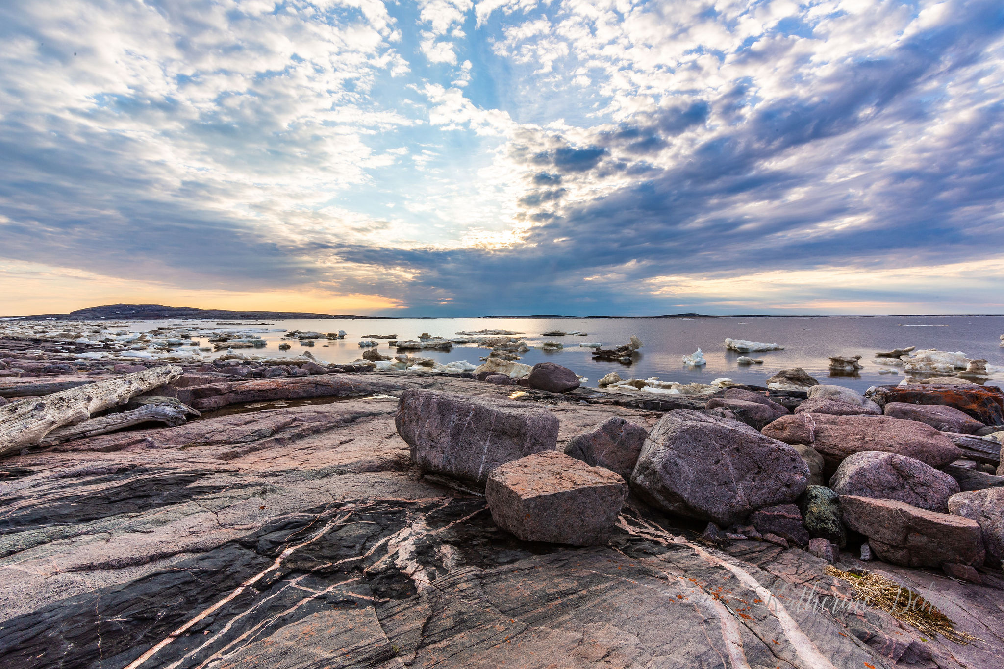 Rocky shoreline and drifting ice along James Bay at sunset