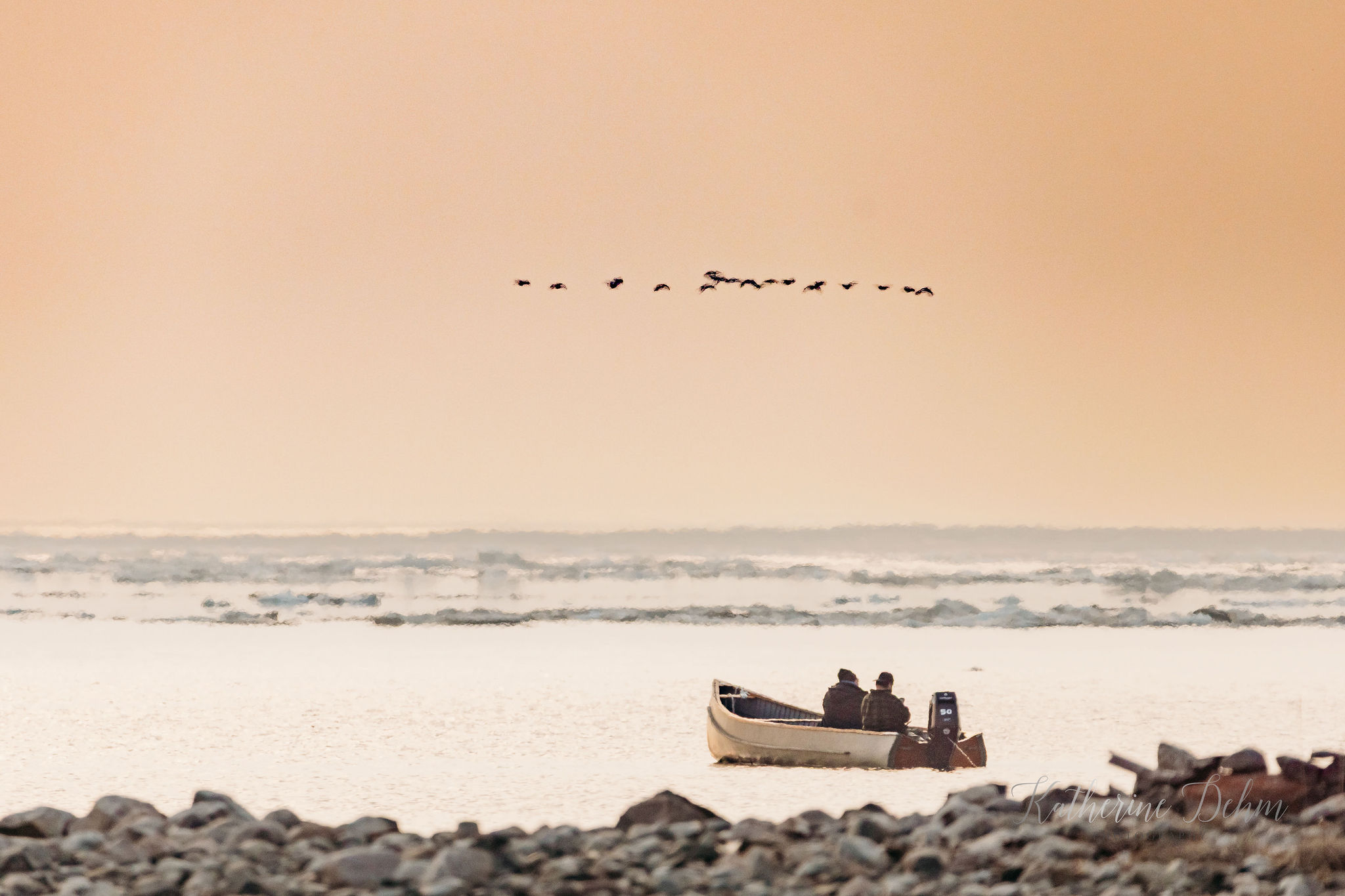 Two hunters in a freighter canoe as geese fly overhead at sunset on James Bay